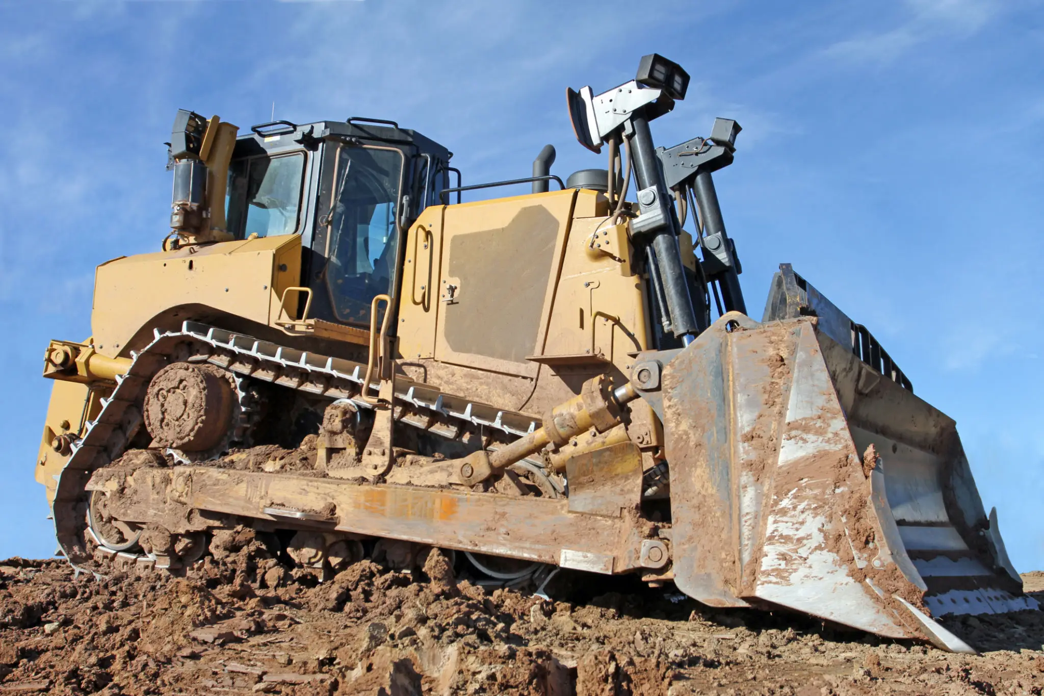 A bulldozer clearing rocky terrain under a blue sky.