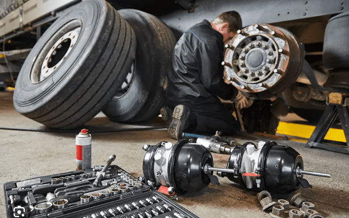 Mechanic working on vehicle parts in a garage filled with tires and tools.
