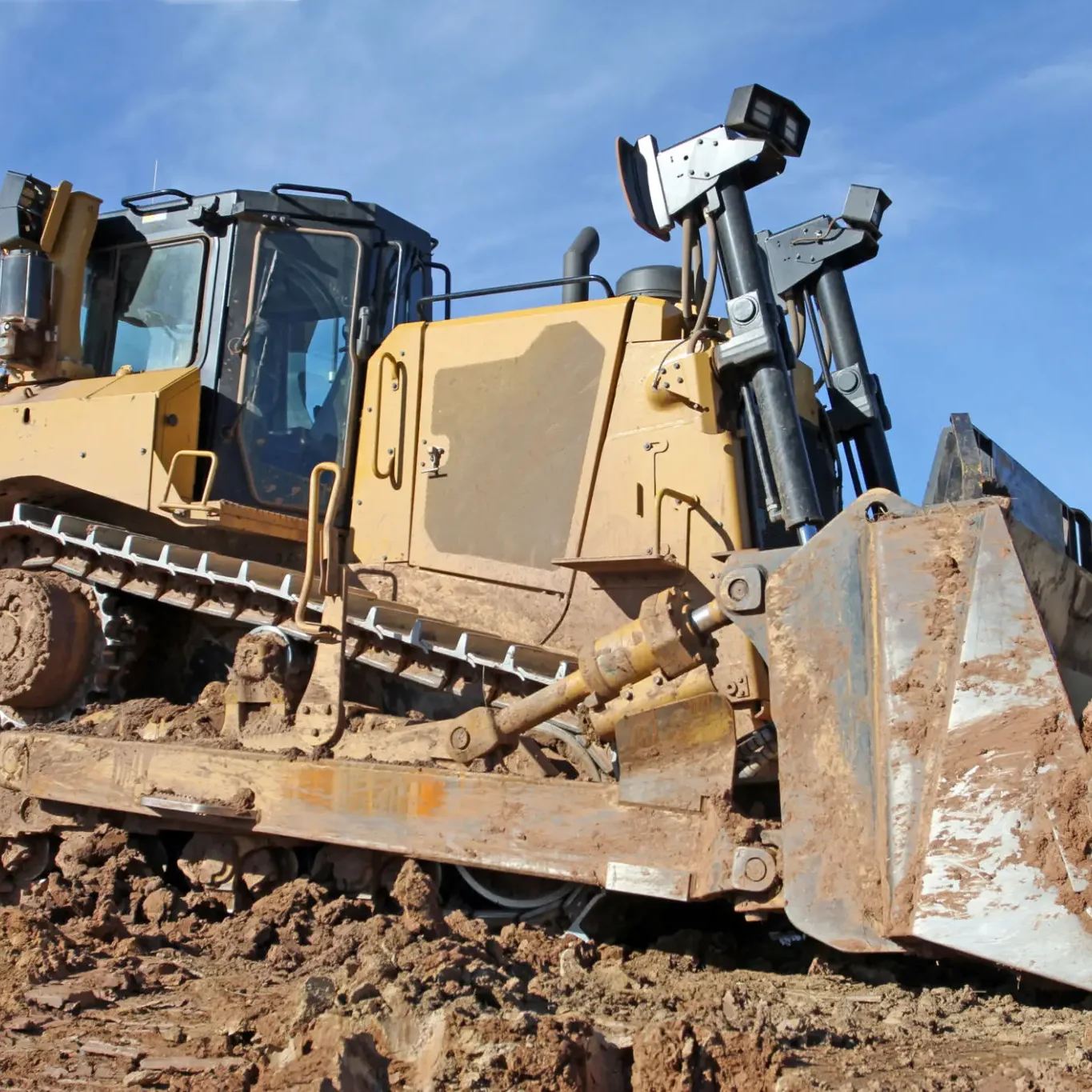A bulldozer clearing rocky terrain under a blue sky.